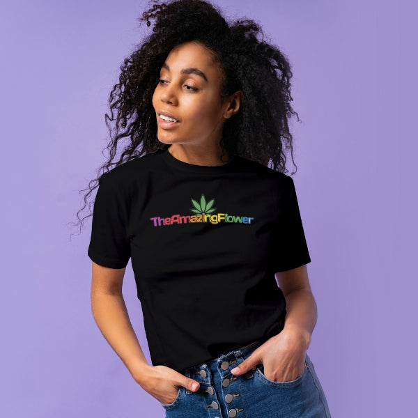 Hemp Leaf Logo Women's T-Shirt from TheAmazingFlower.com (Black) worn by a black woman against a light lavender background. She is looking to her right with her hands partially in the pockets of her blue jeans